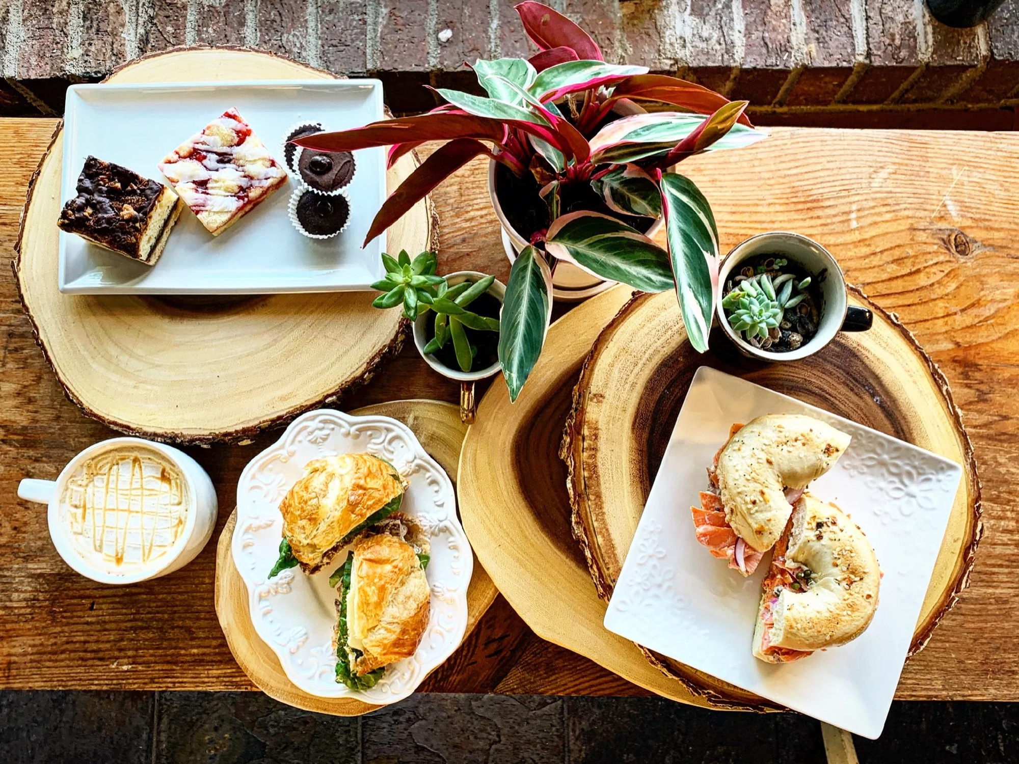 Overhead flat lay of sandwiches, pastries, and coffee on a wood table at Moments Coffee Bar & Eatery